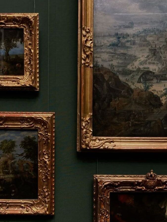 Multiple ornate gilt-framed paintings hung on a deep green wall, depicting landscape and pastoral scenes.